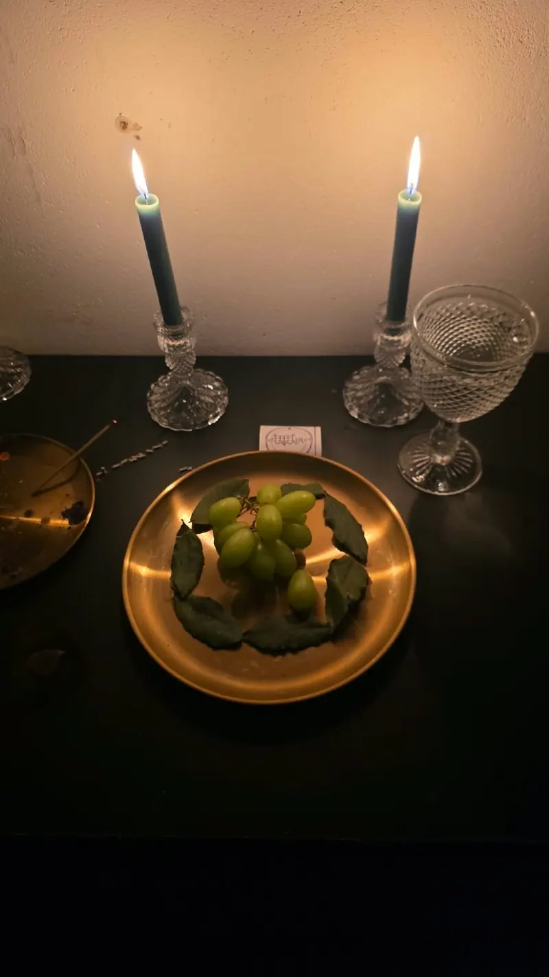 Altar com duas velas verdes, taça de cristal e uvas num prato dourado